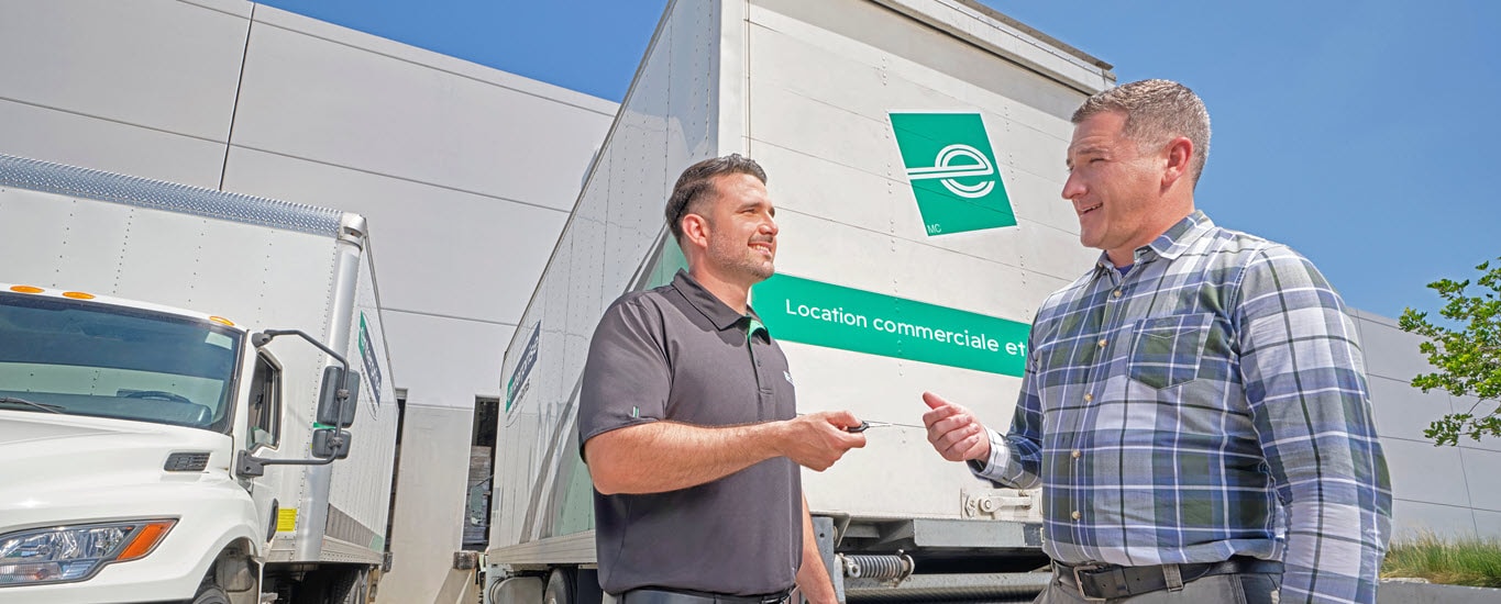 Homme poussant des boîtes sur un diable devant un fourgon colis Enterprise